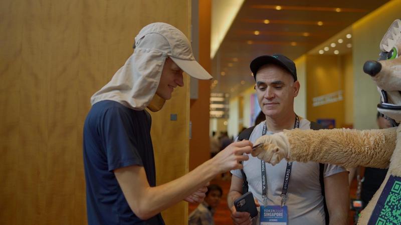 Vitalik Buterin receiving branded condom from GraphDex hedgehog mascot